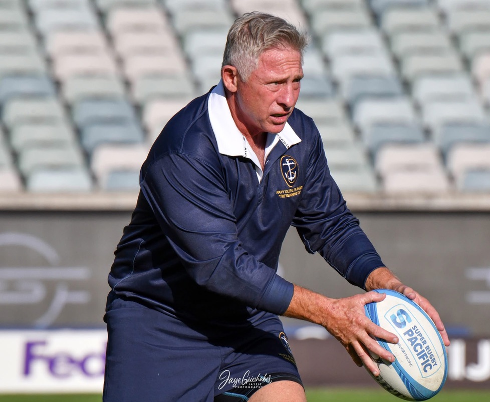 Will Collett in a navy rugby jersey holding a rugby ball on a stadium field