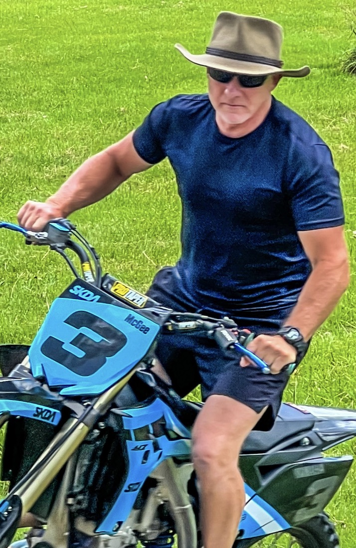 Will Collett riding a dirt bike across grass, wearing a broad-brimmed hat