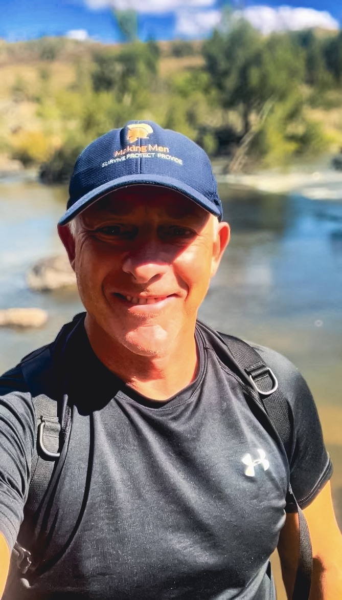 Will Collett wearing a Making Men cap, standing beside a river on a sunny day